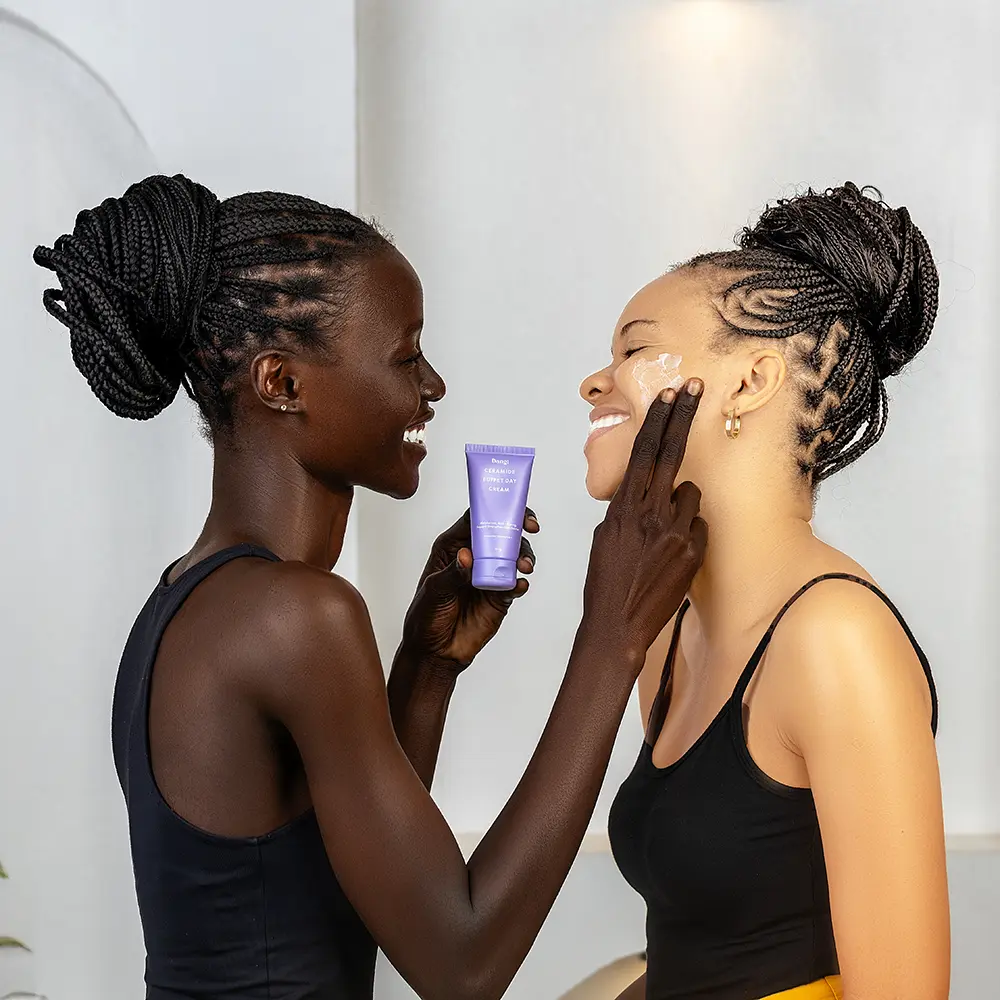 2 female models smiling at each other while applying skincare product